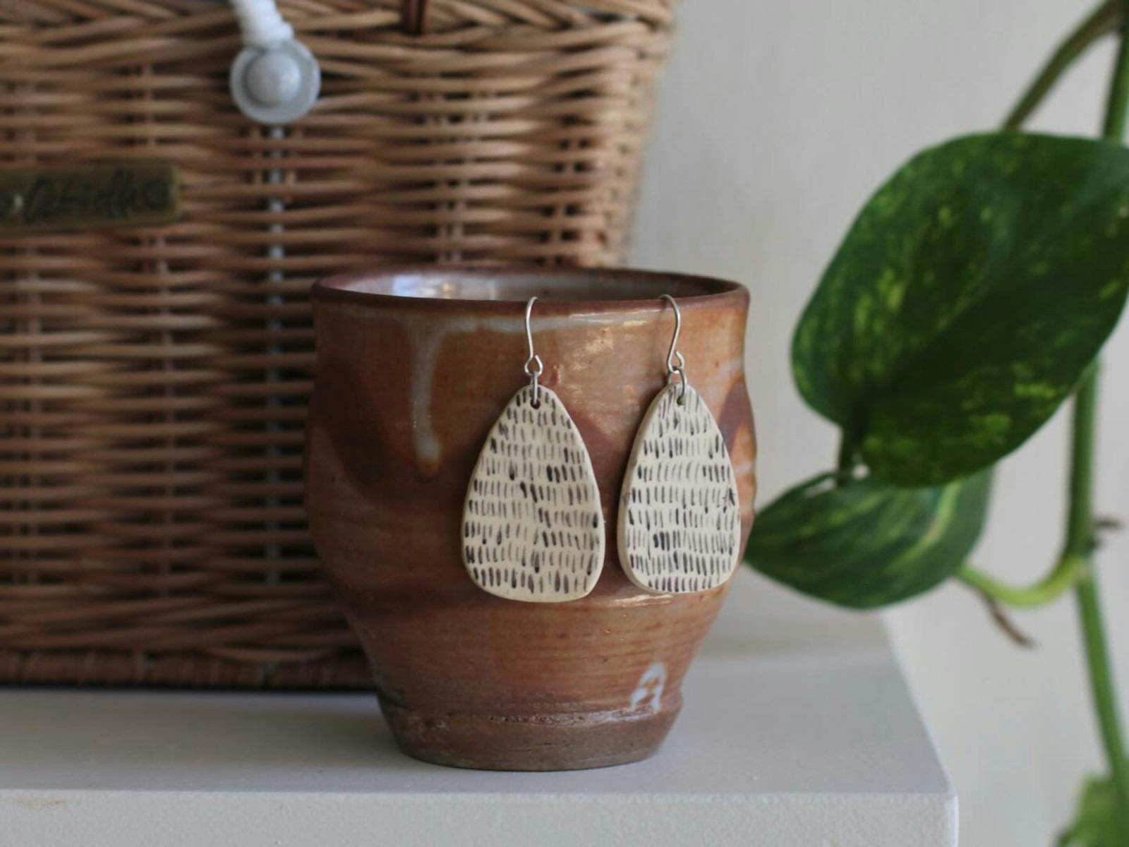 a pair of earrings hanging on a brown mug with a basket in the background