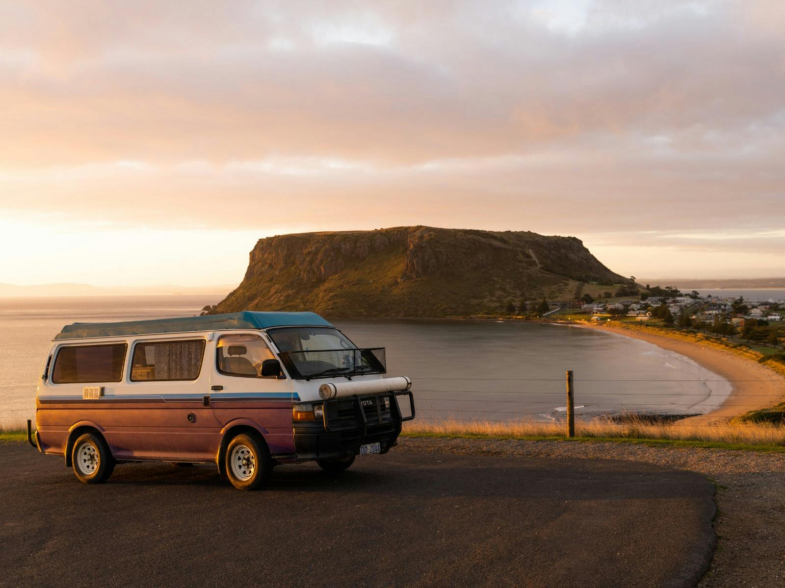 A campervan is parked in a carpark overlooking the beach in Tasmania