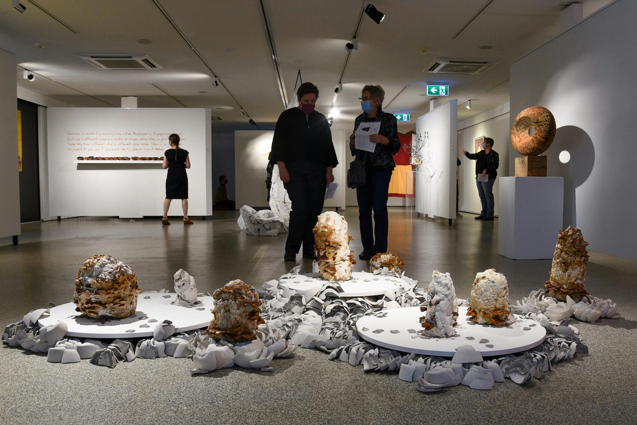 Two people standing over an installation artwork of mushroom micellium and ceramics on the floor.