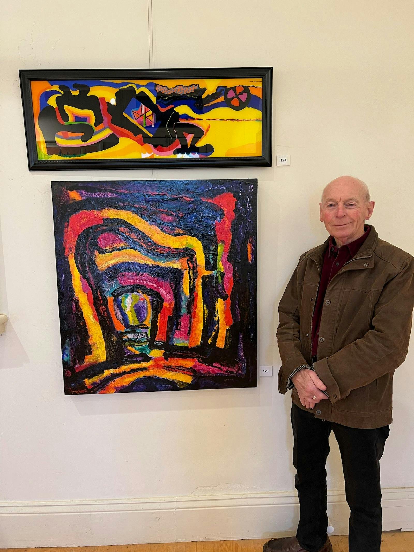 Russell is pictured with 2 of his dynamic, colorful abstract acrylic paintings.