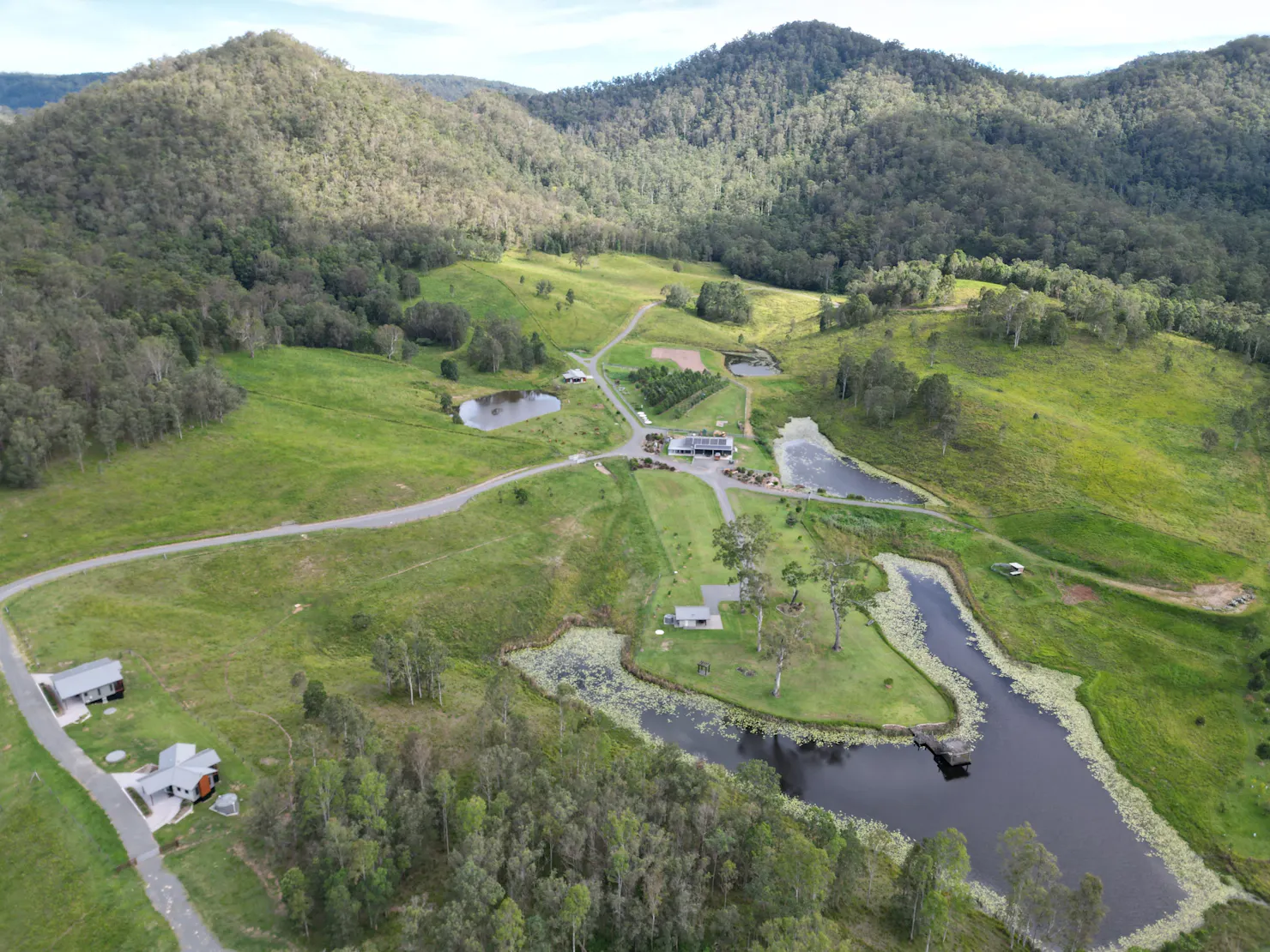 Drone view of farm with lodges, dams, roads, and forested hills in the background