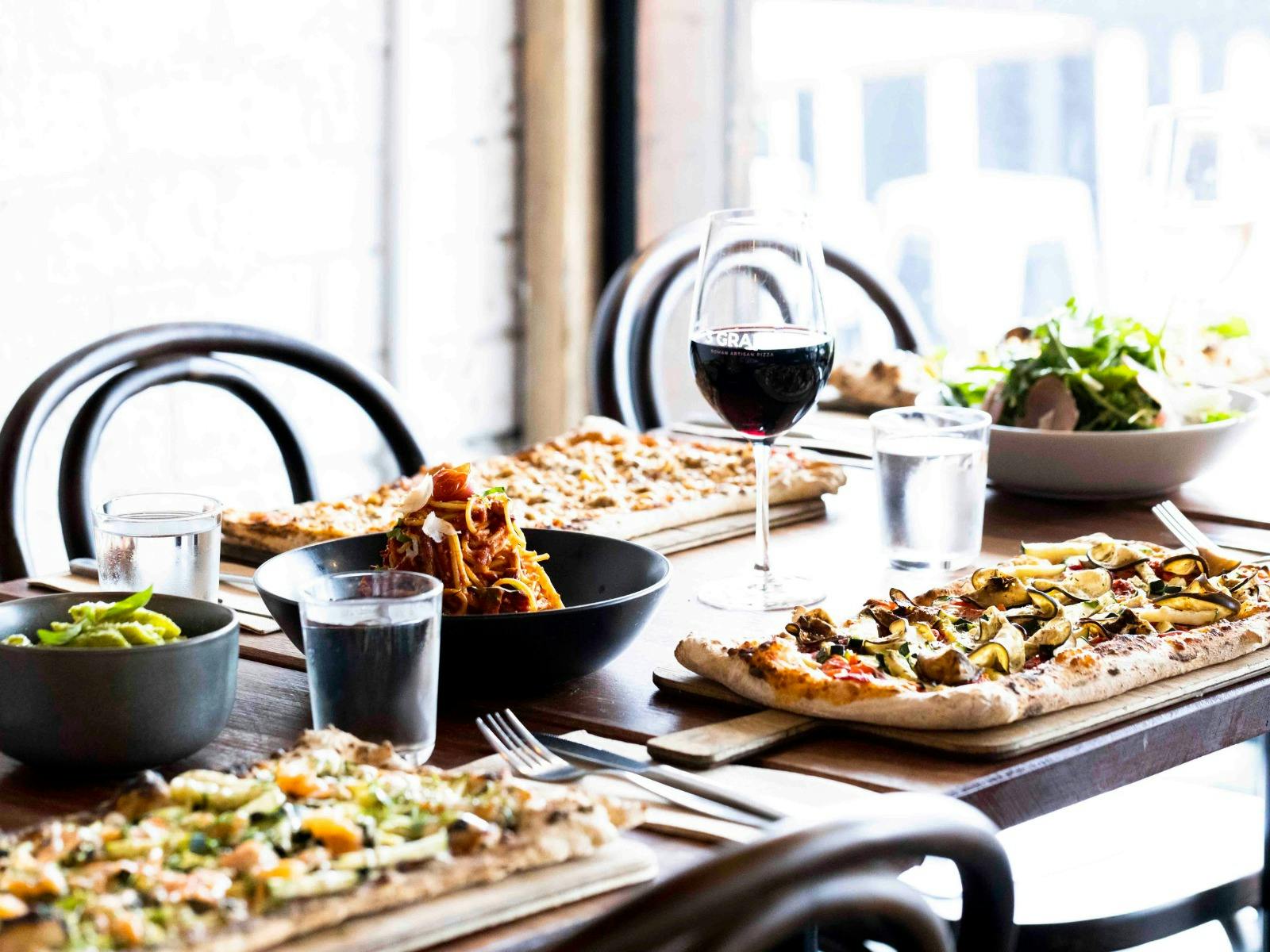 a table with pizzas, pastas and salad with wine glasses