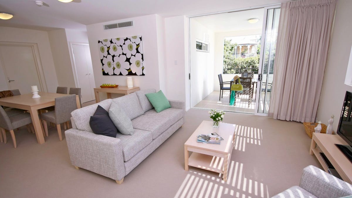 Light-filled open-plan living room with sofa, coffee table, dining area and sliding doors to a priva