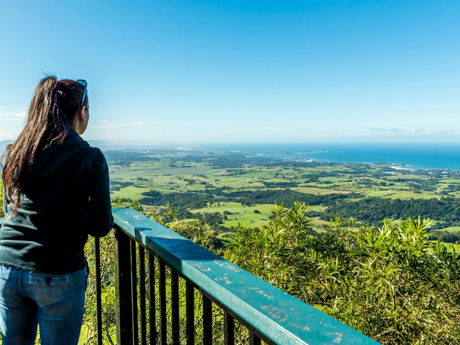 Girl against safety fence looks out over green valleys that meet the ocean
