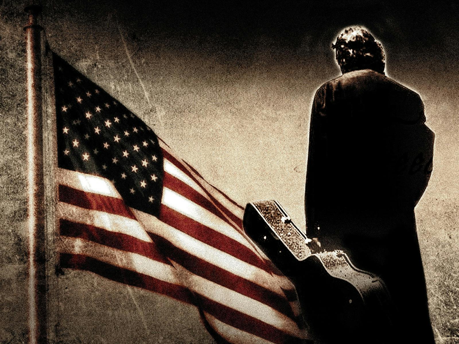 American Flag with man dressed in black with a guitar case