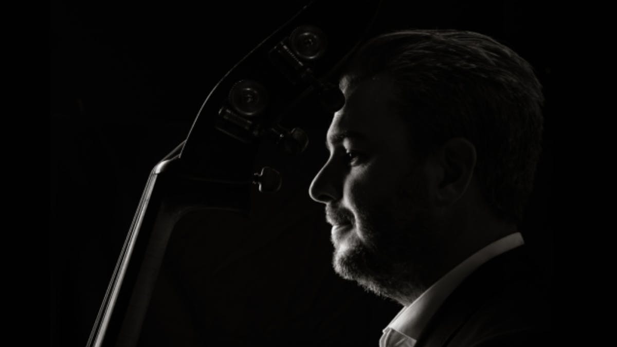 Black-and-white portrait of a double bass player in profile, looking toward the light