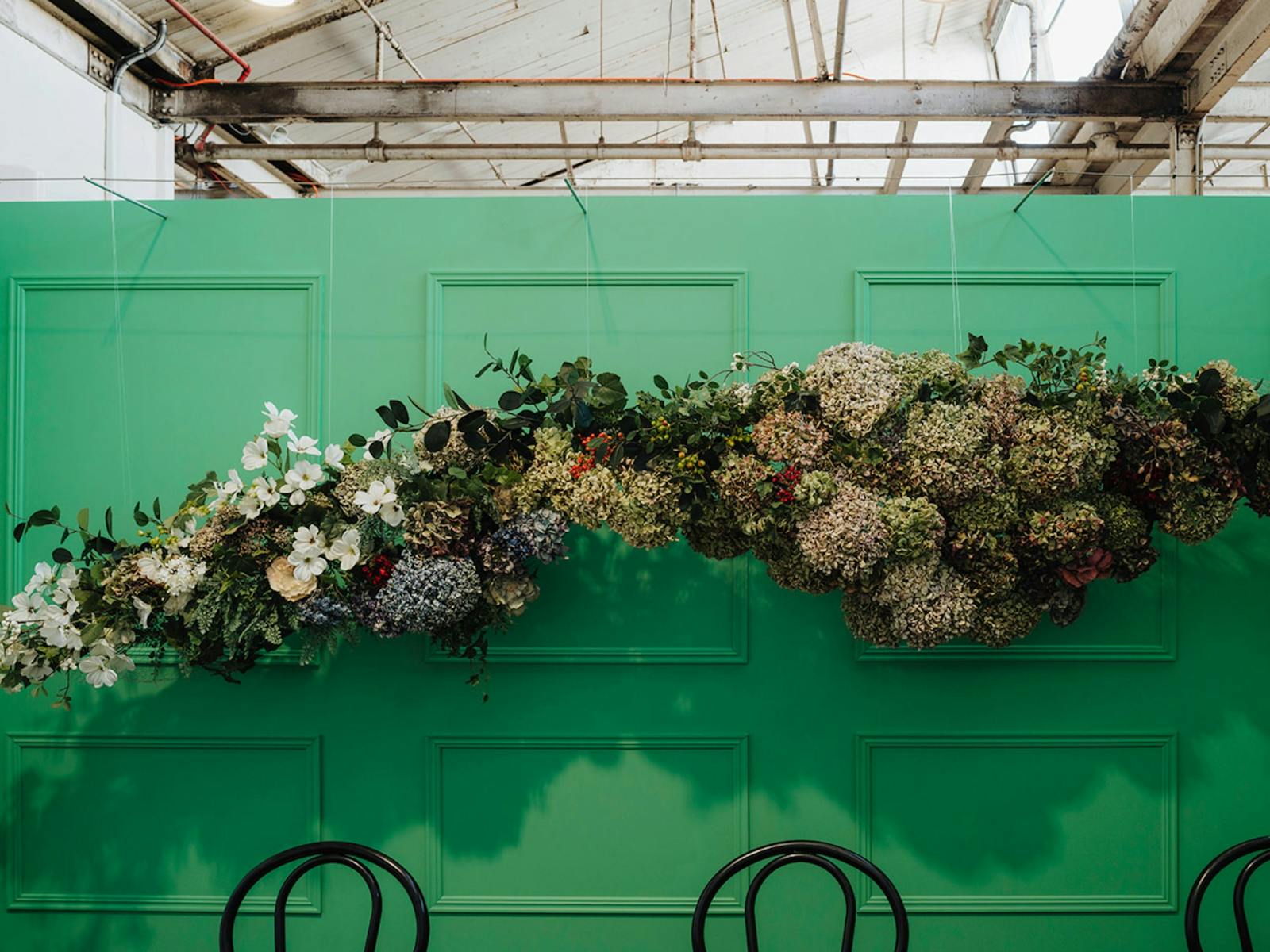 A hanging floral arrangement above black chairs and a bright green wall inside the Aysha Hansen venu