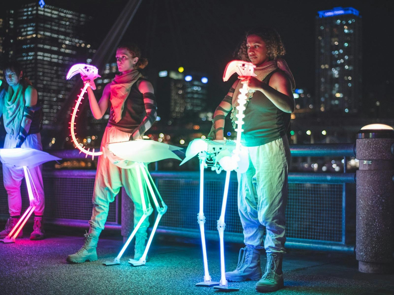 Two puppeteers operate rainbow LED flamingo skeletons