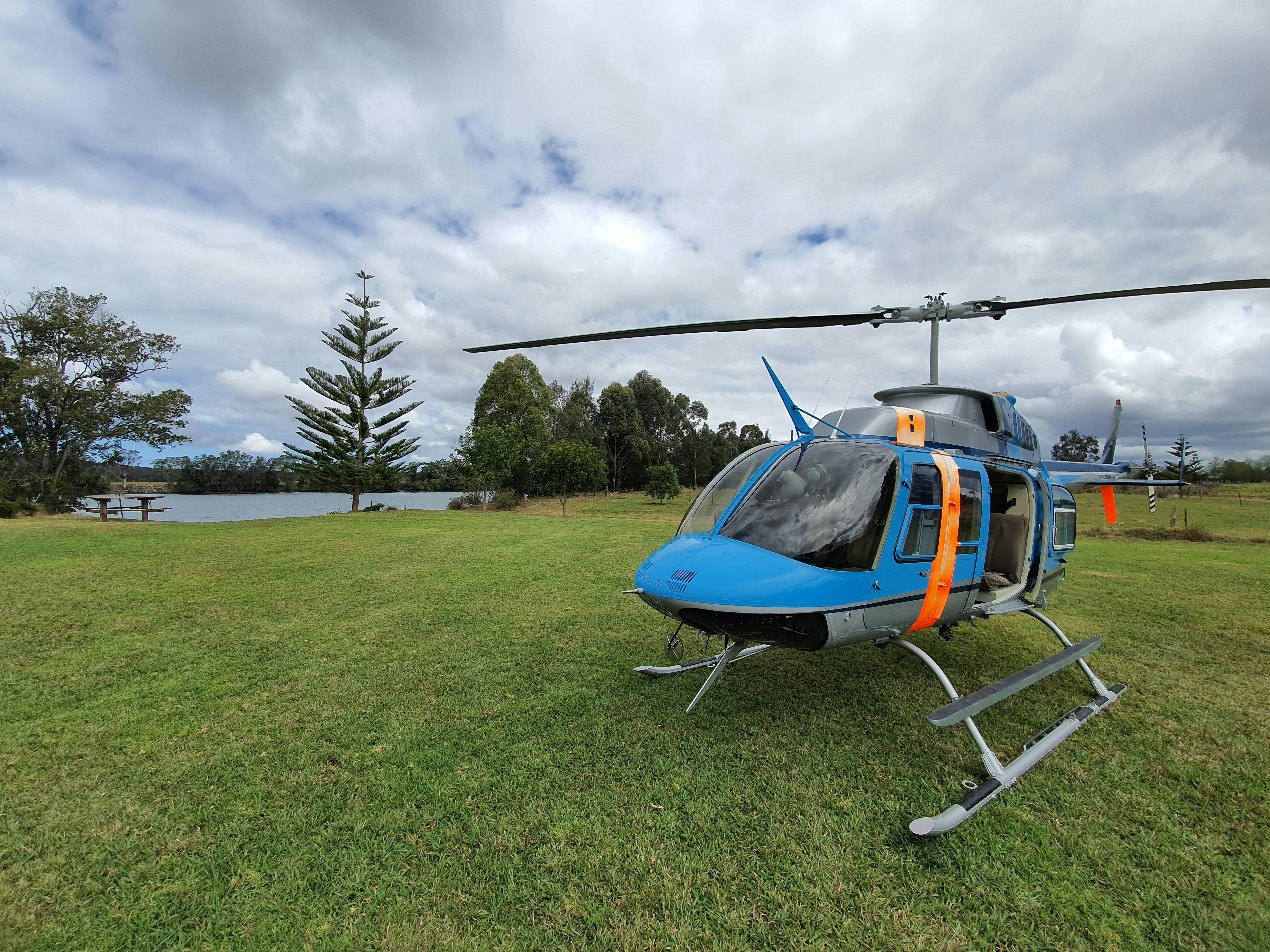 Helicopter landed on lush green grass with a river and trees in the background