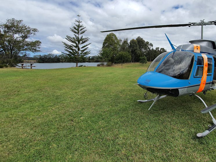 Helicopter landed on lush green grass with a river and trees in the background