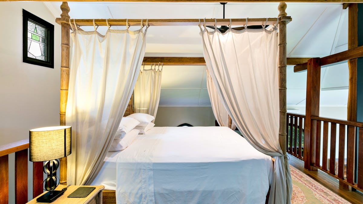 Interior shot upstairs bedroom. Queen bed with canopy curtains. Dark wood furniture, white linens
