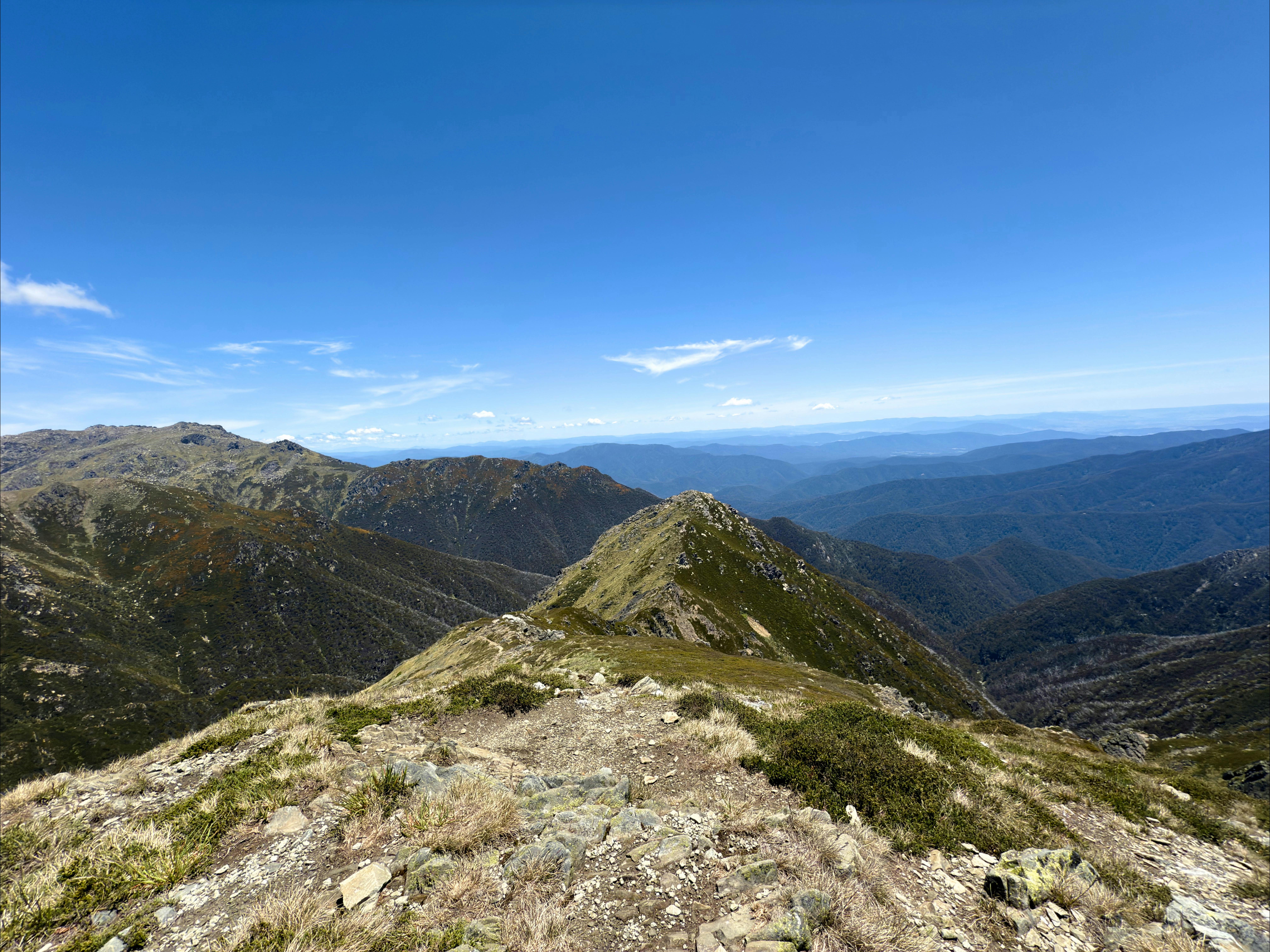A narrow ridge with mountains in the distance and a blue sky.