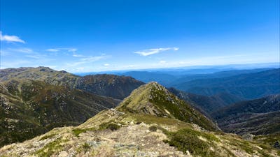 A narrow ridge with mountains in the distance and a blue sky.