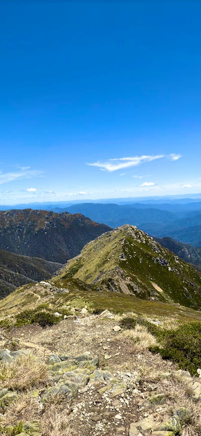 A narrow ridge with mountains in the distance and a blue sky.
