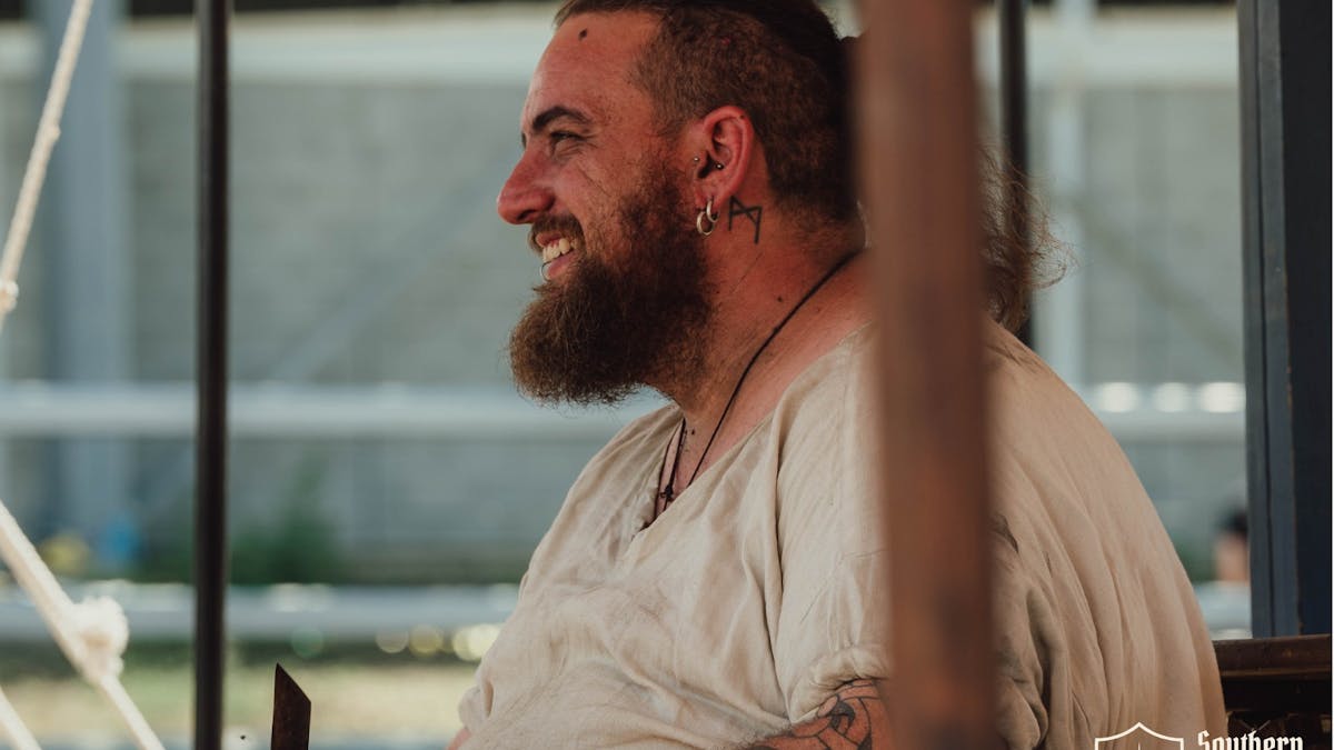 Smiling bearded medieval reenactor at the Southern Realm Festival encampment.
