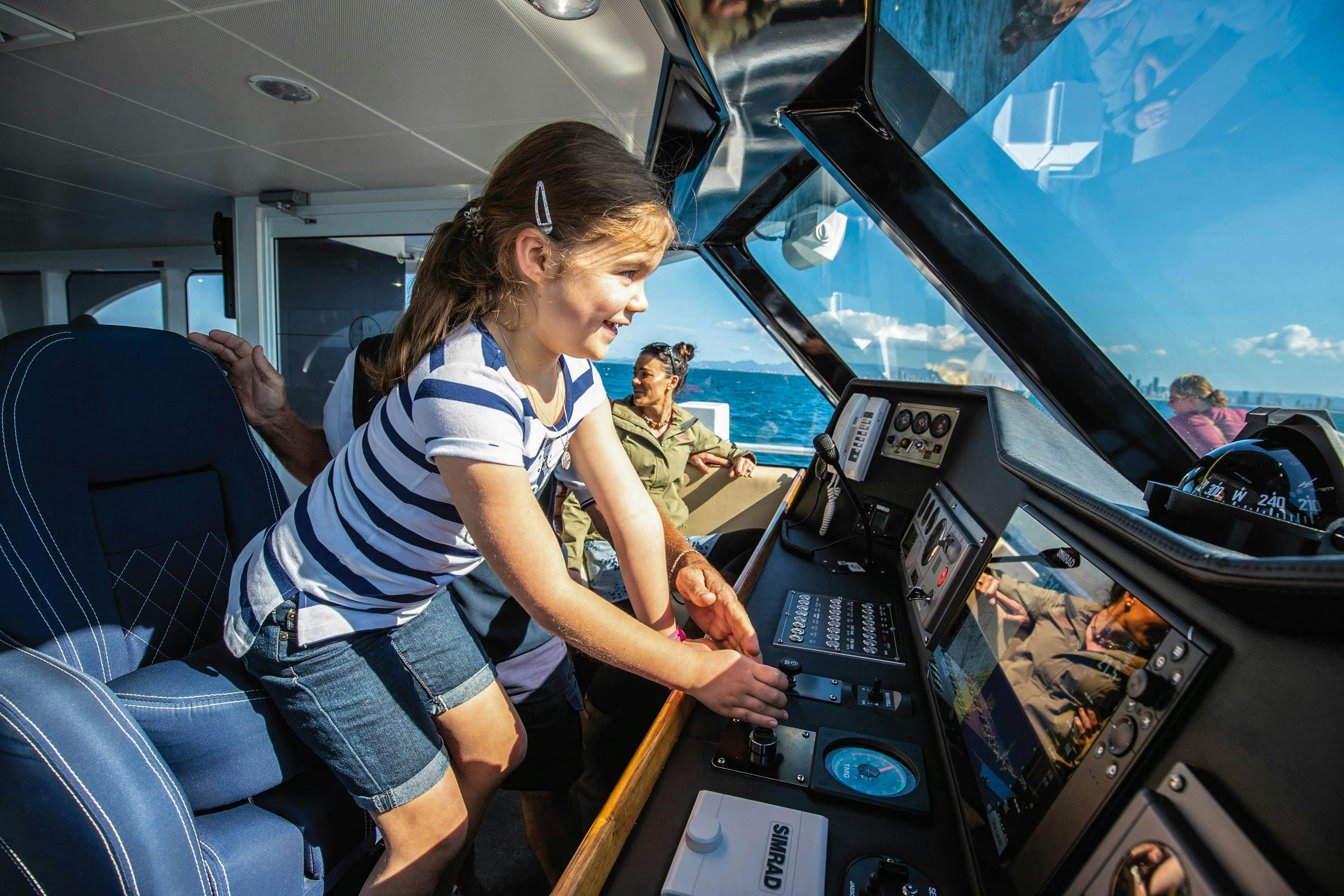 Excited young girl at helm of boat next to boat skipper