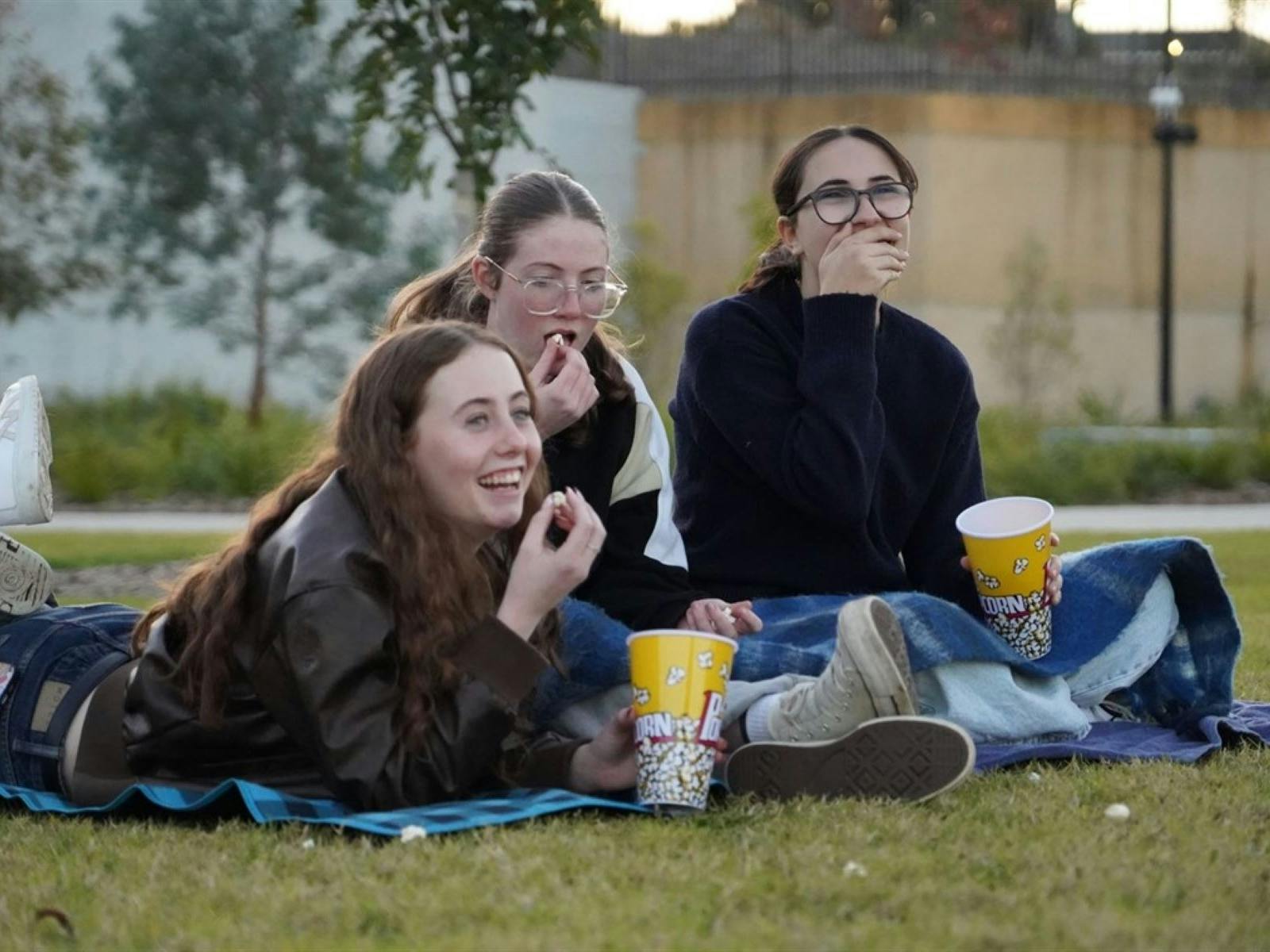 Three girls sitting on a blankets eating popcorn and laughing