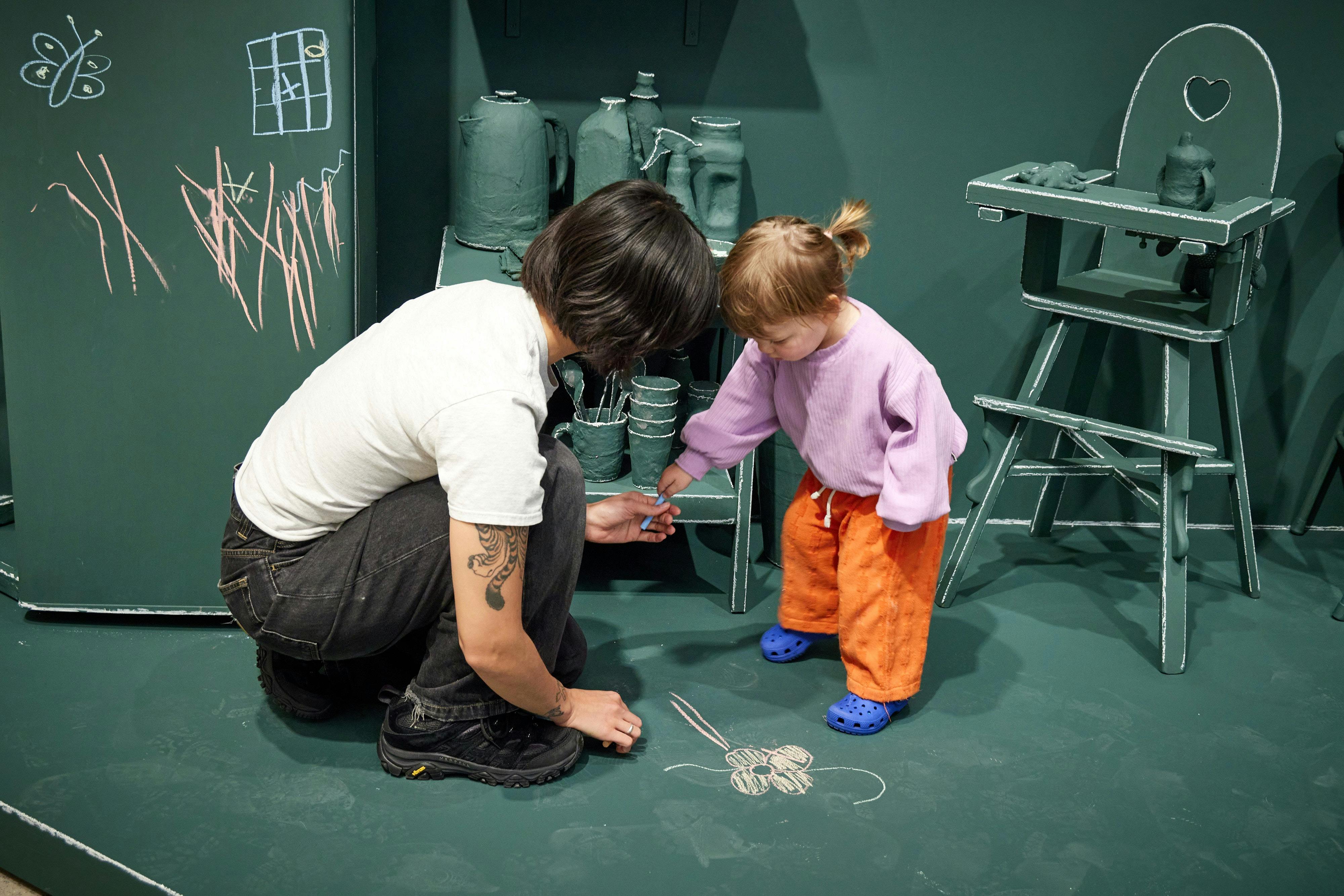 A child and her mother drawing a flower wiht chalk in an interactive echibition in the art gallery
