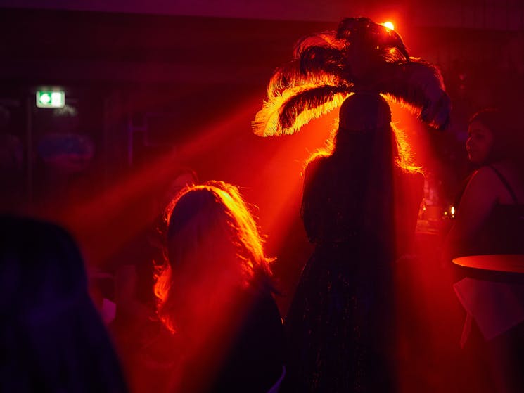 Showgirl head dress surrounded by orange stage lighting to give theatrical silhouette