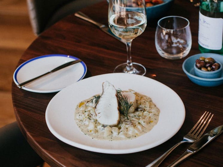 fish fillet in white sauce on wooden table with a glass of wine and cutlery at rick stein restaurant