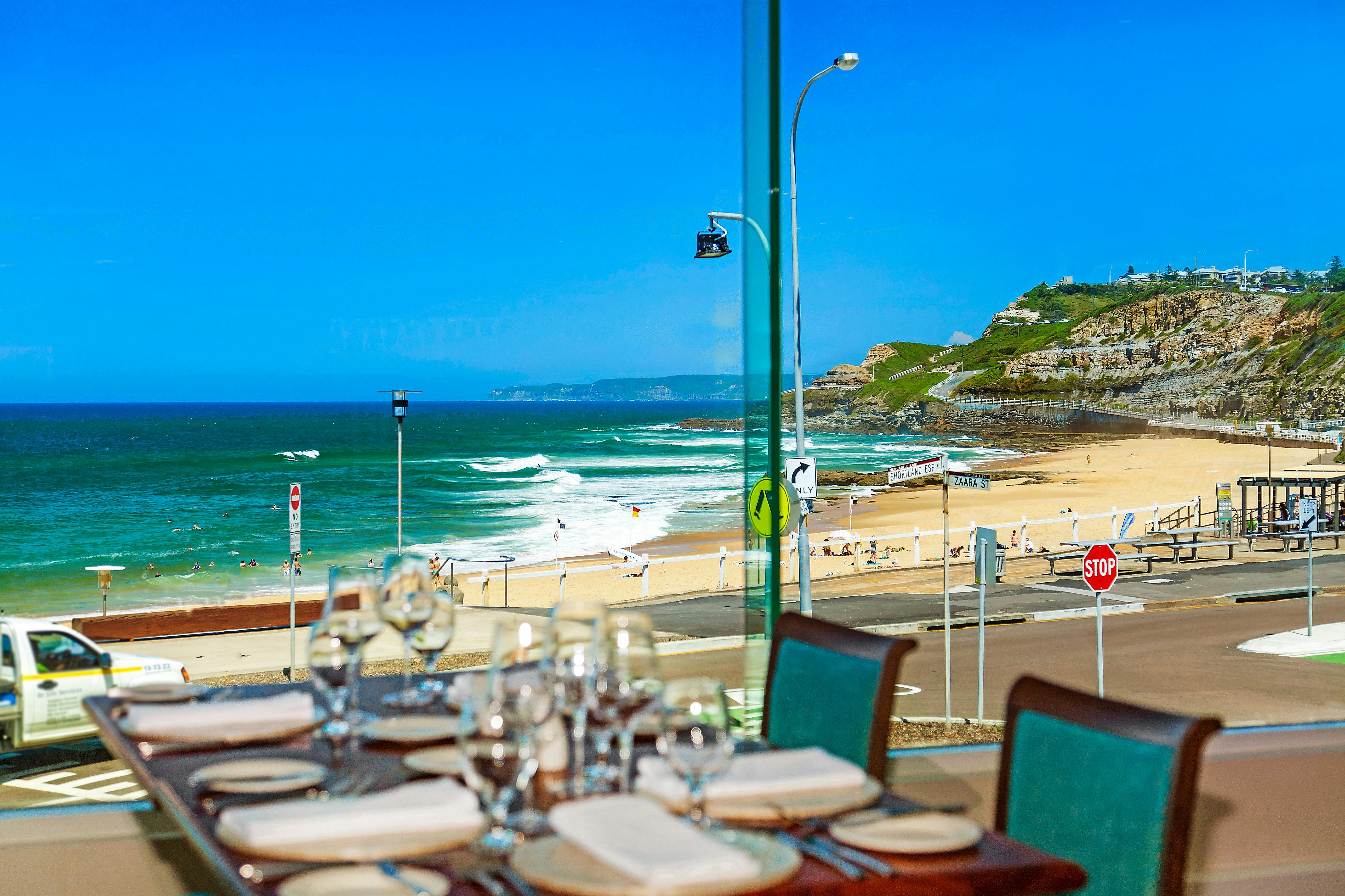 Table set with glassware and plates. View overlooking Newcastle beach