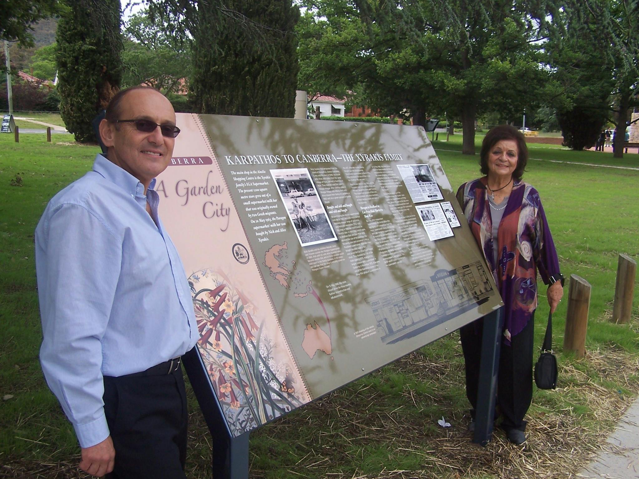 Man and woman standing at either side of sign outdoors in park.