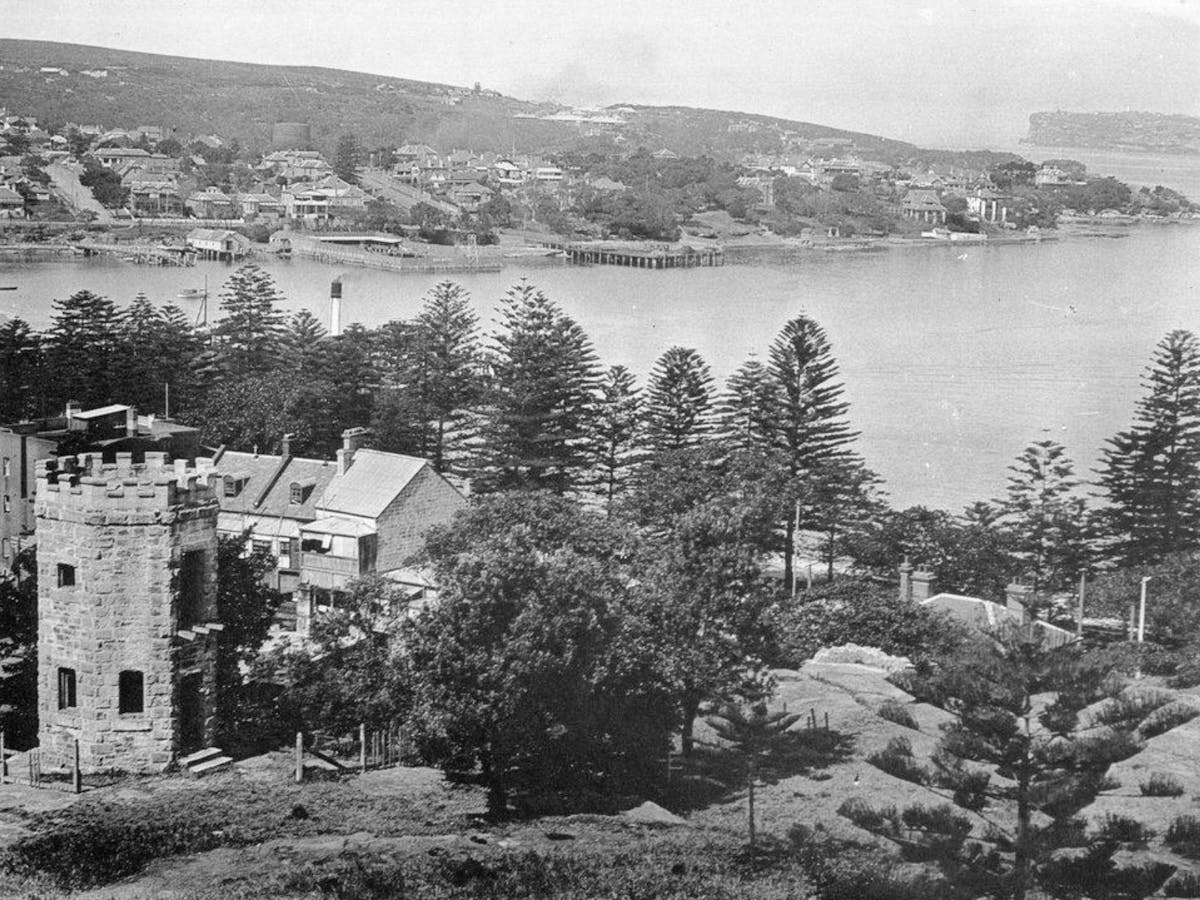 Old black and white image with buildings in the foreground infront of the waters of Manly