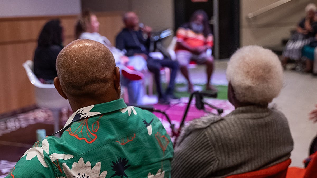 Framed from behind 2 people watching a talk in the Queensland Museum Theatre