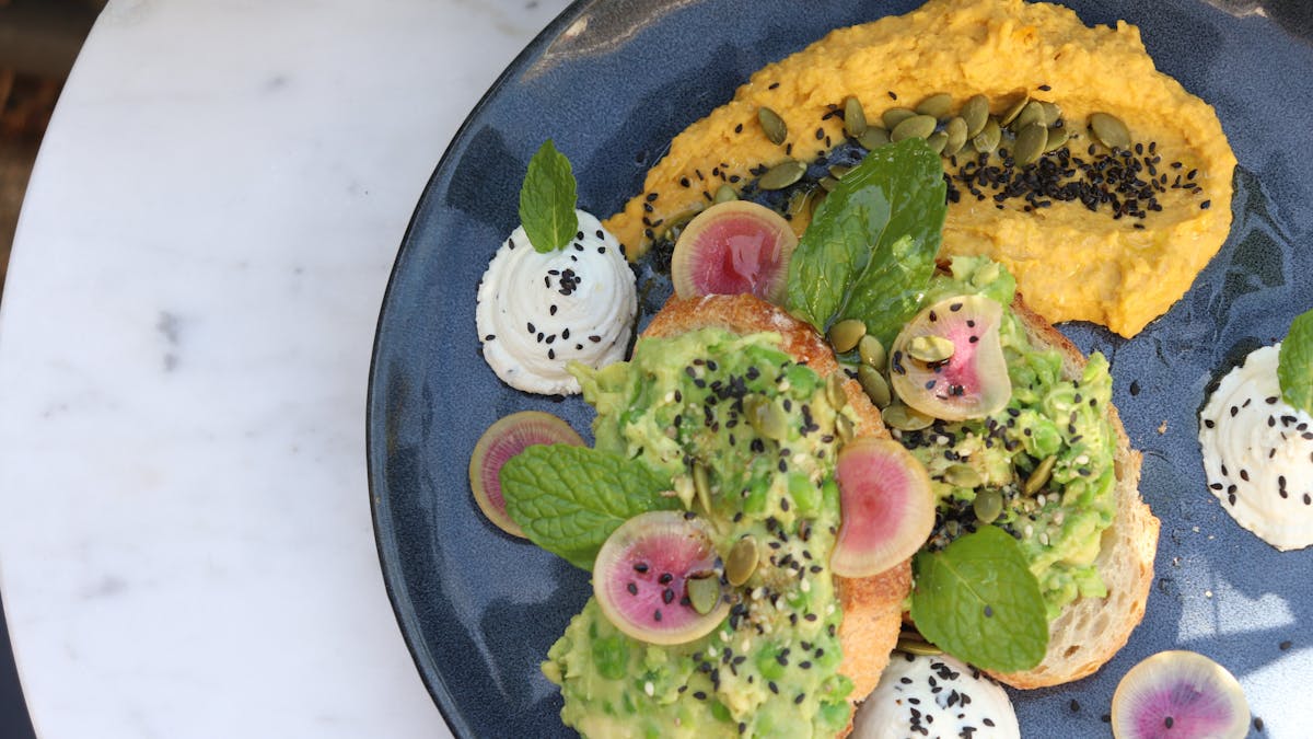 Avocado on sourdough toast with a generous smear of pumpkin hummus and dollops of whips goats curd.