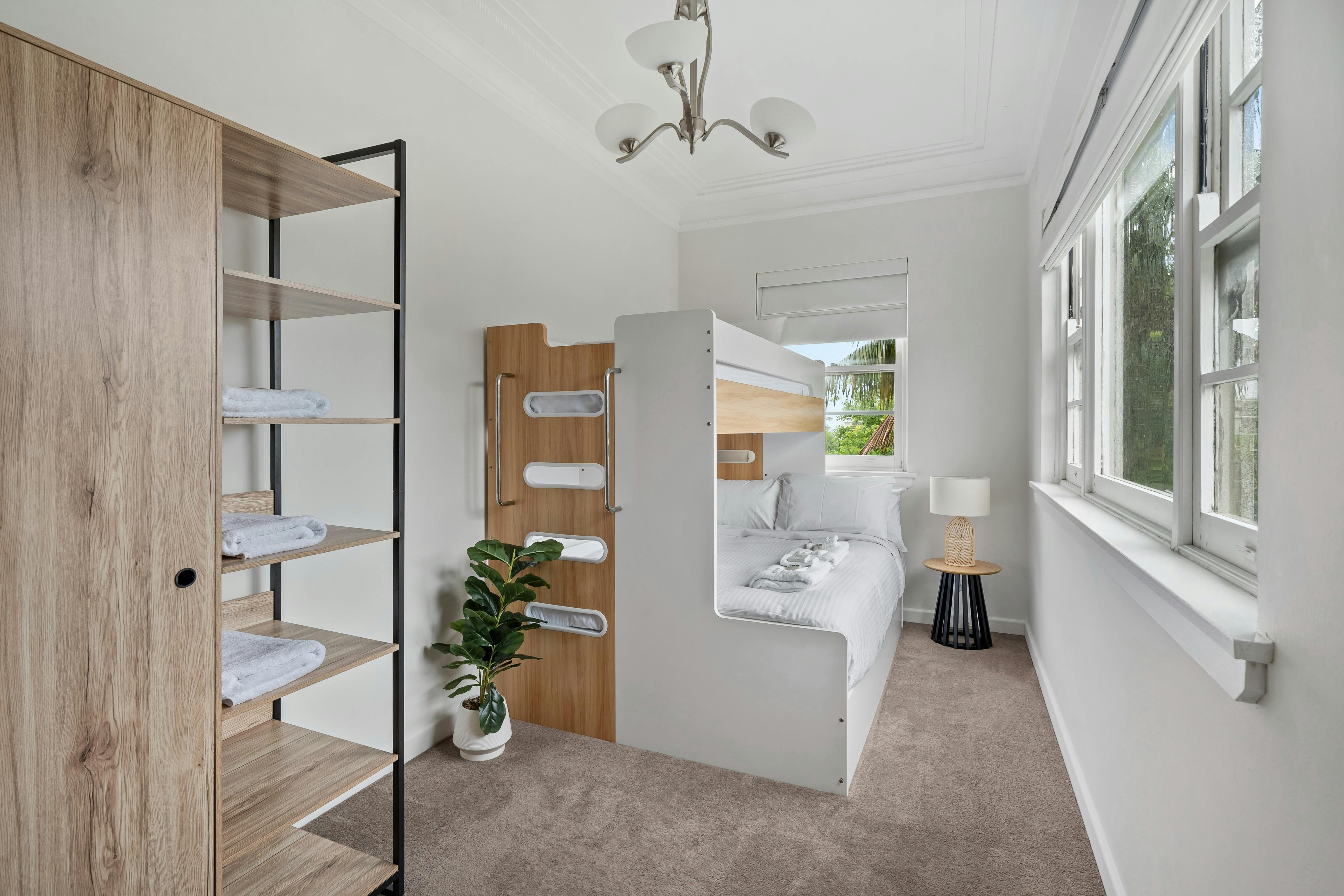 房间里有一张双层床和现代化的储物架，明亮的自然光透过窗户照进来。