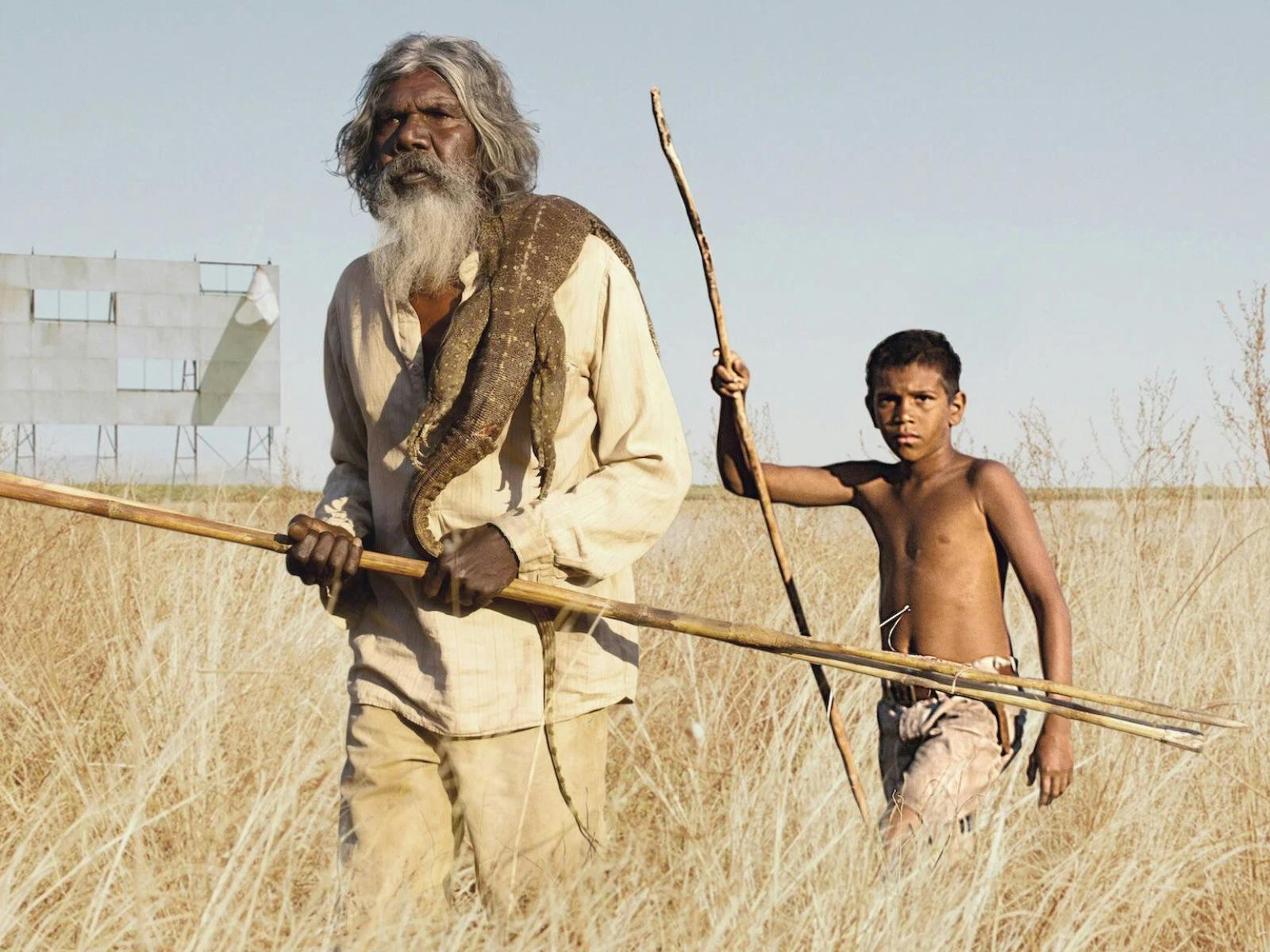Older Aboriginal man and Aboriginal boy walking through long grass in the sun