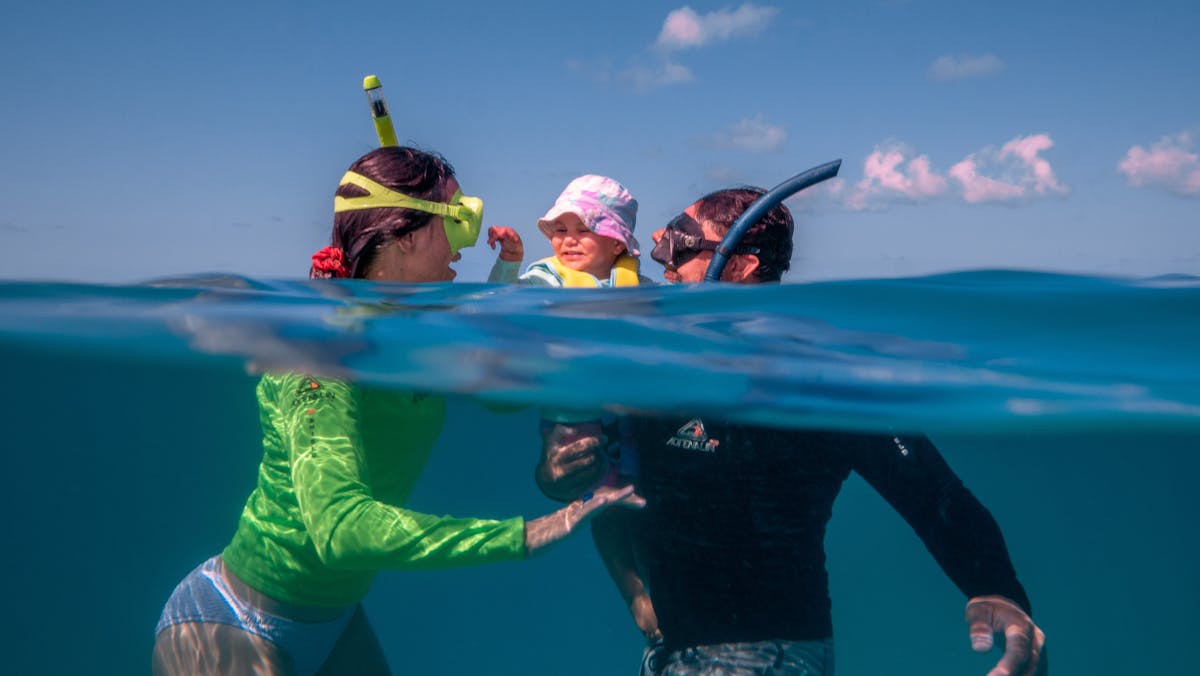 A man and women are snorkelling with their child.