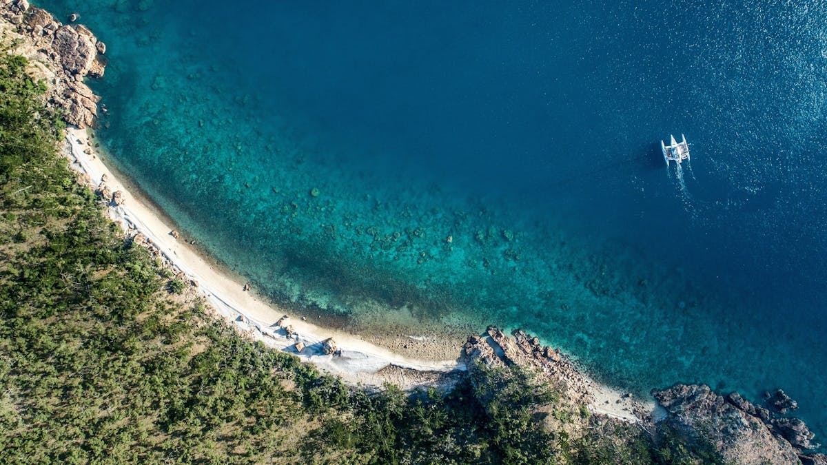 Aerial photo of secluded beach and rocks in Blue Peal Bay with coral visible under water and a boat