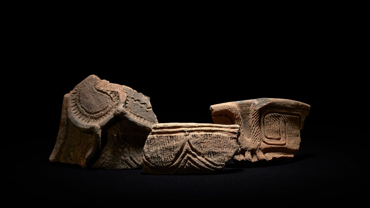 Three pottery fragments dramatically illuminated on a stark black background Three pottery fragments dramatically illuminated on a stark black background
