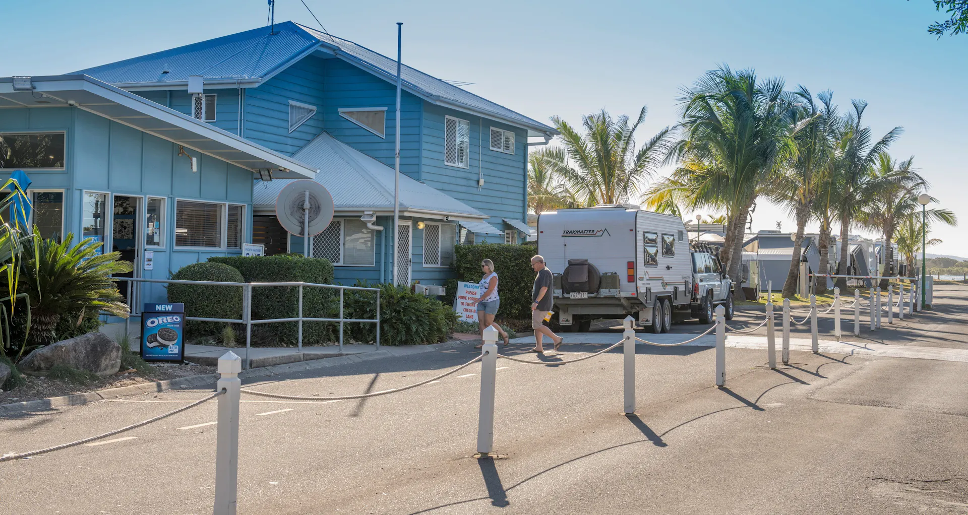 Image of Cotton Tree Holiday Park Office. Wide shot with caravan and couple walking in to office.