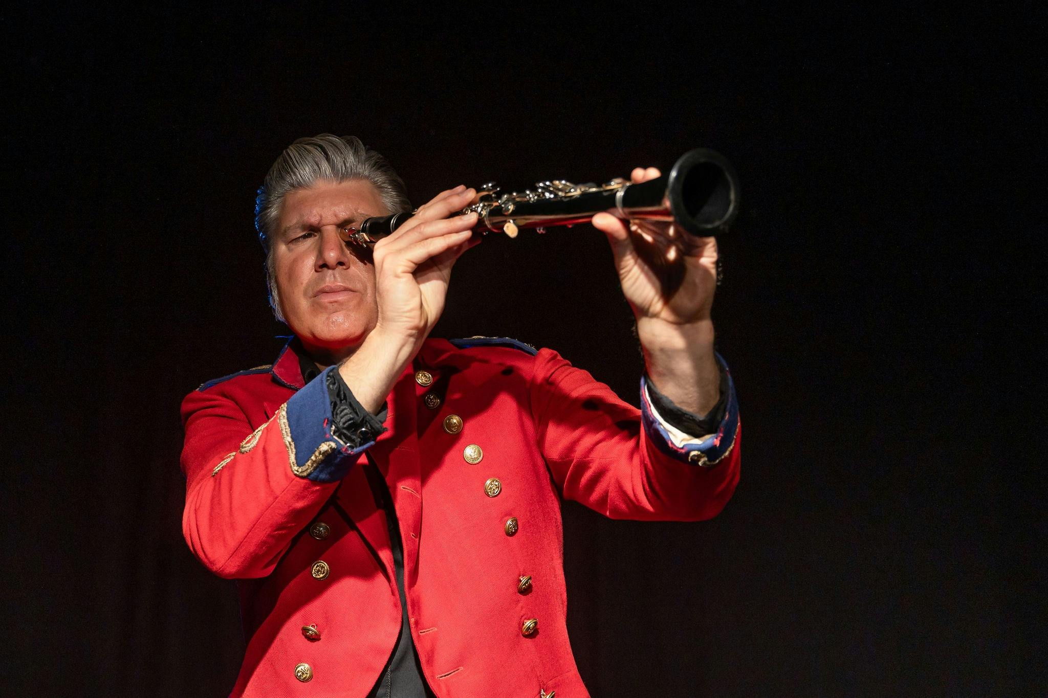 A man dressed in a red suit looking through a telescope.