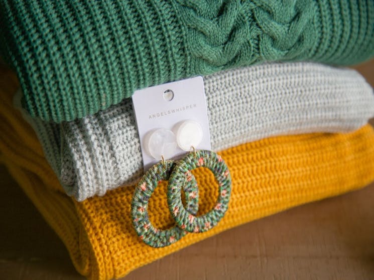 Green, blue and yellow folded jumpers with blue and yellow hooped earrings leaning on them