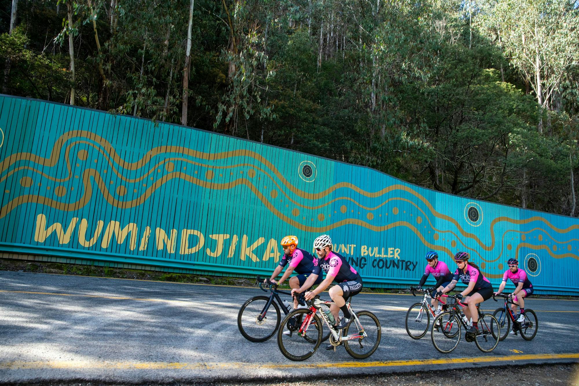 Group of cyclists riding past the Mt Buller welcome sign