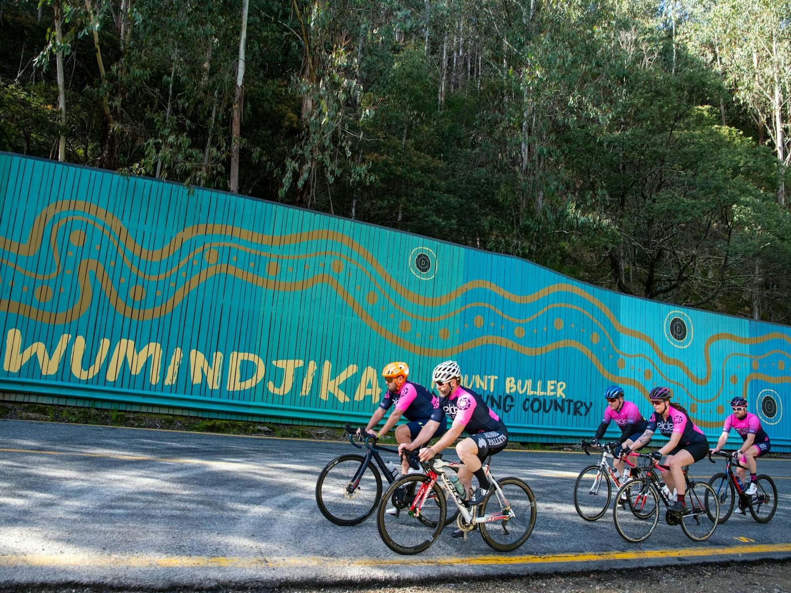 Group of cyclists riding past the Mt Buller welcome sign