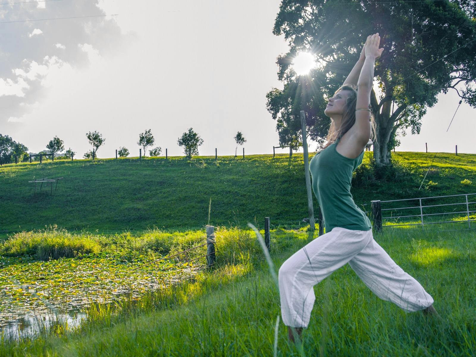 A young woman stretches in a yoga pose on a green lawn by the hillside