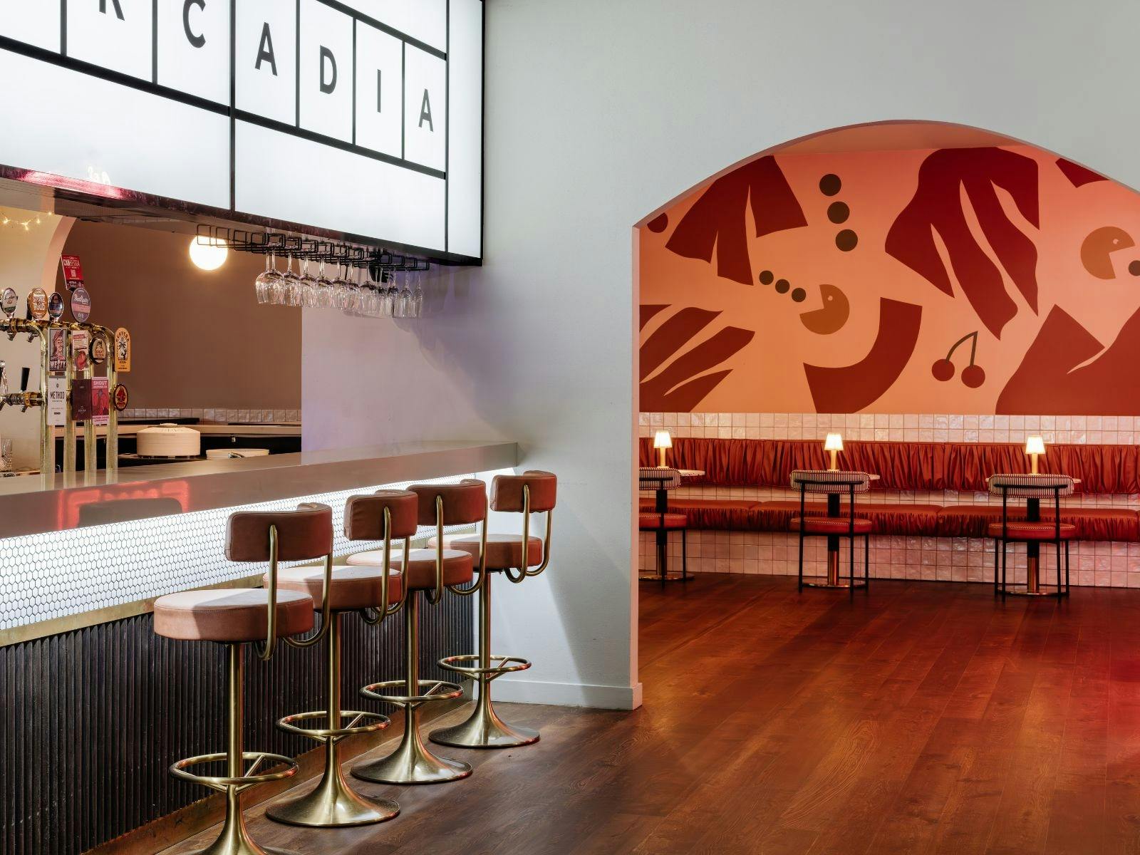 A bar with brown stools and a room with a pink Pacman-inspired wall mural