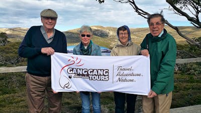 four seniors holding a gang gang tours banner with mountains behind