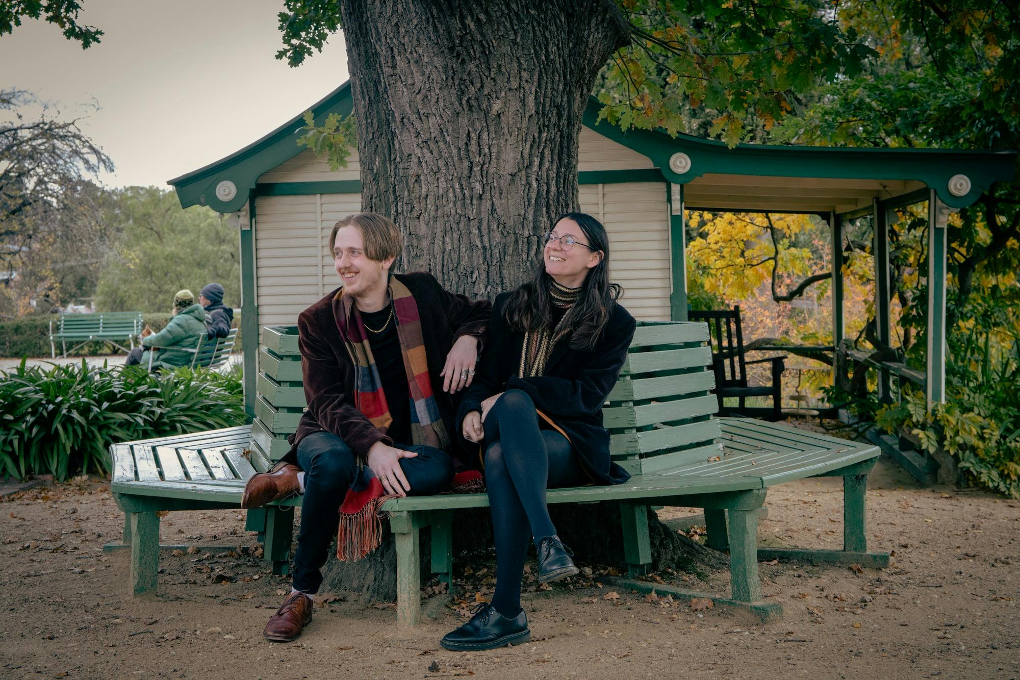 Two people sitting on a bench under the tree
