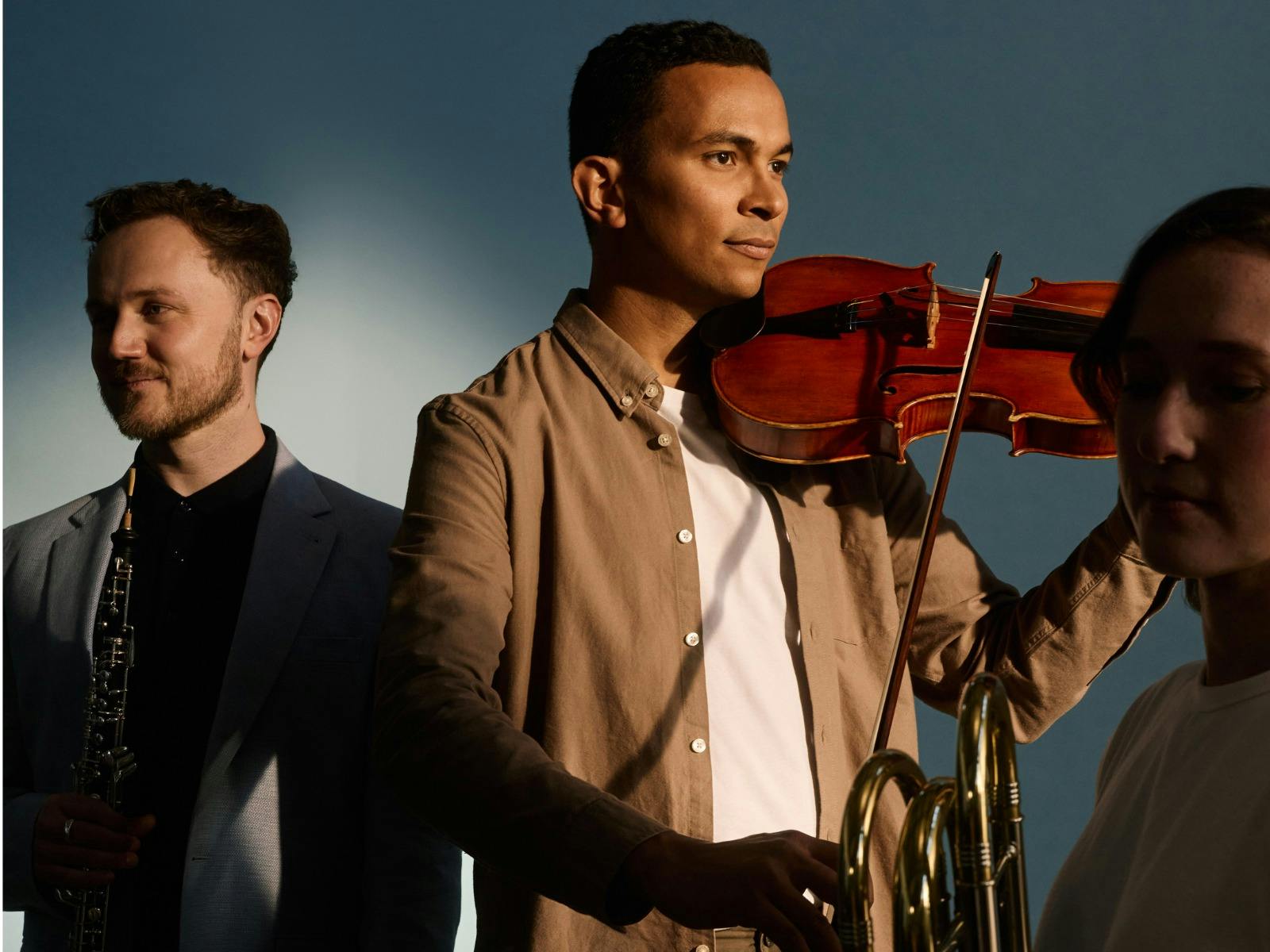 A photo of three ASO players holding instruments, facing different directions, in a studio setting.