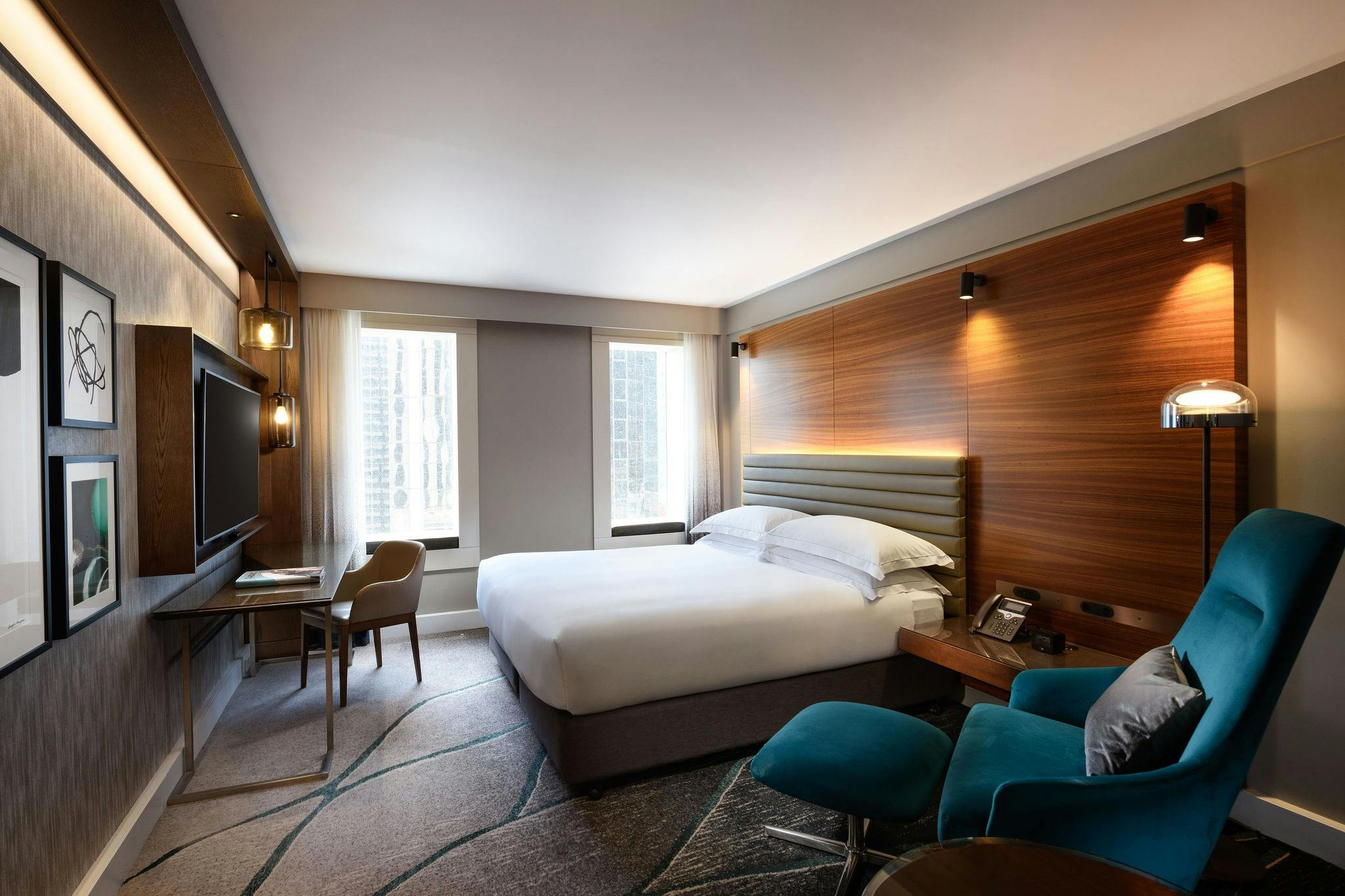 A King Guest Room at Hilton Sydney. You can see the plush king bed, tv, desk and chair with ottomon.