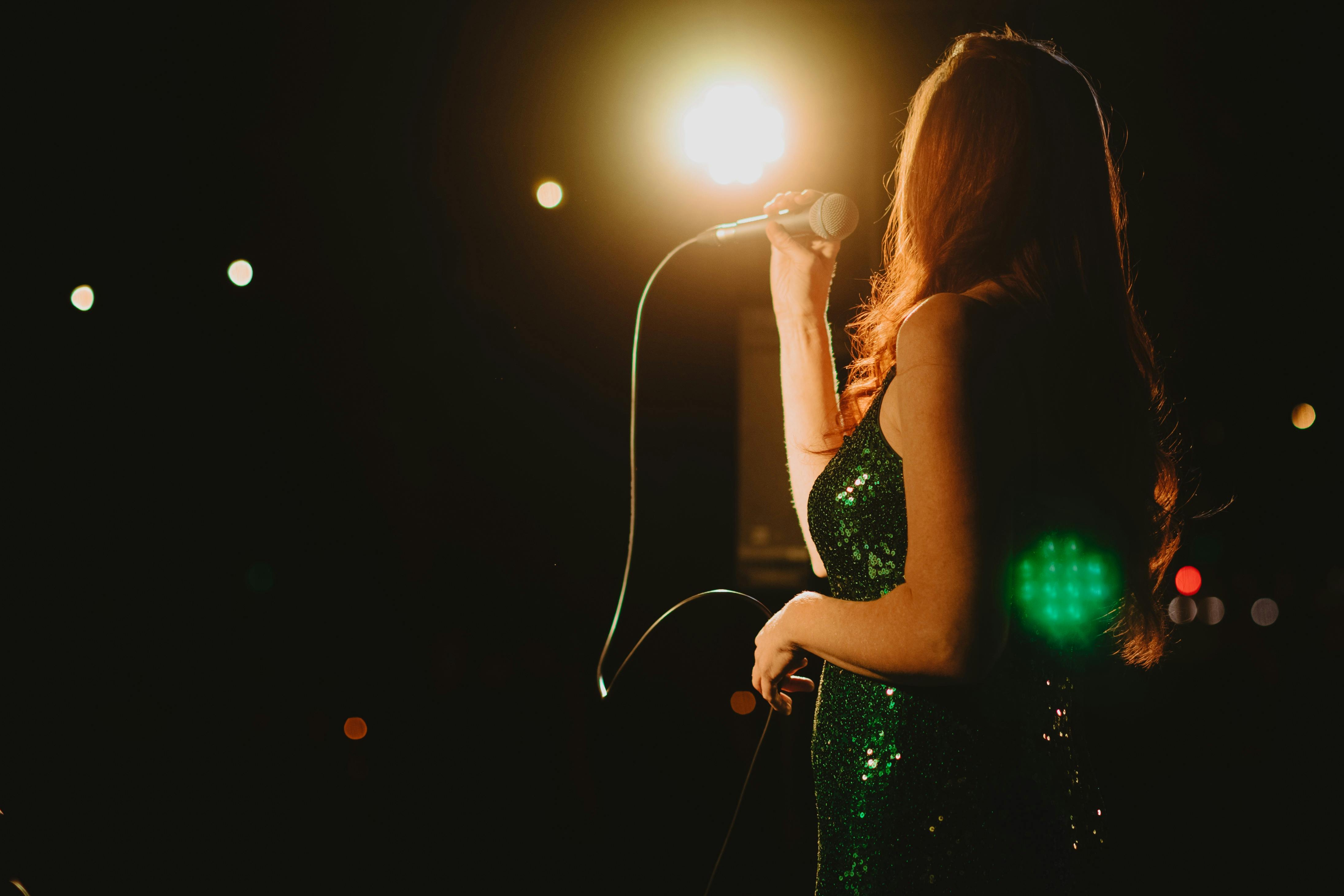 A woman standing and talking into a microphone wearing a green dress. The background is dark.