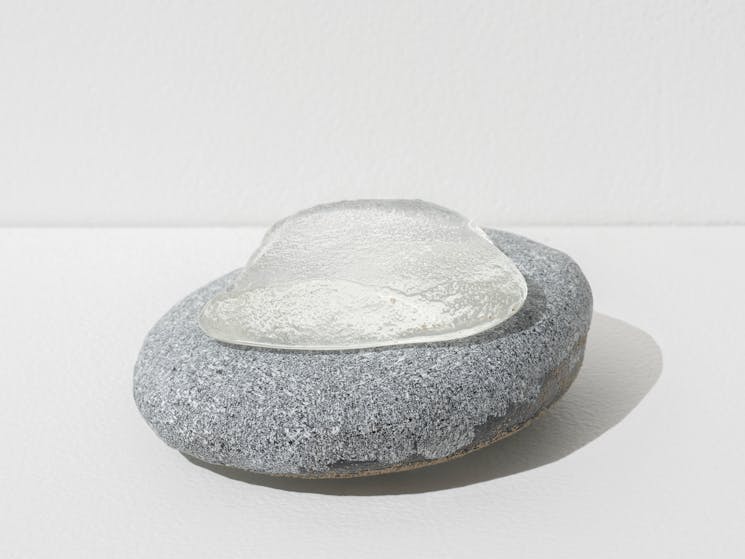 A clear glass giba (grinding stone) resting on natural grey stone