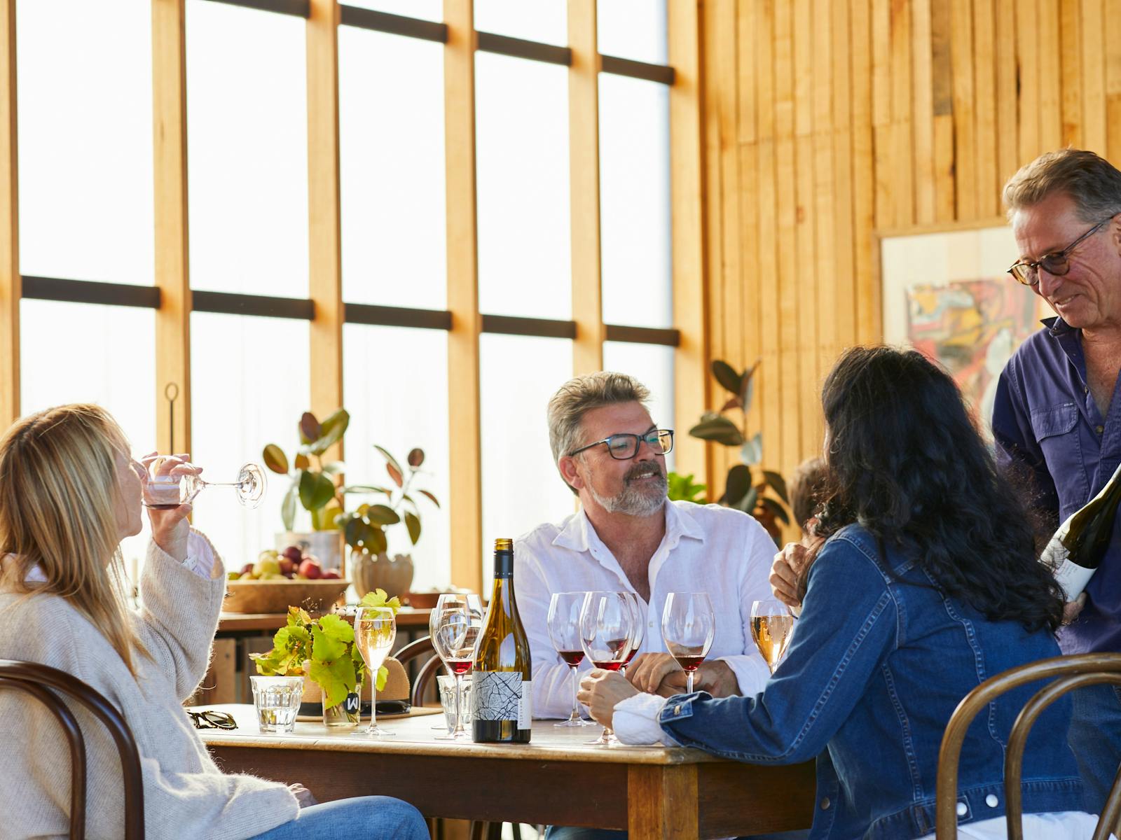 People enjoying a wine in our Tractor Room; Lined in Tasmanian Oak with a fire & bathed in sunlight