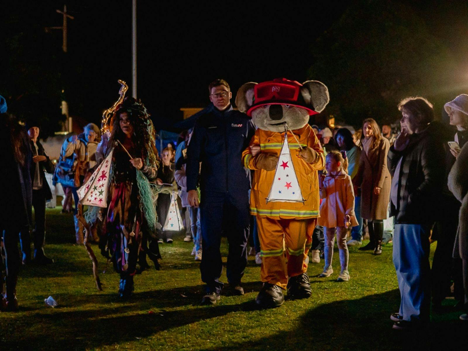 CFA Captain Koala walking with lantern and people at night in parade