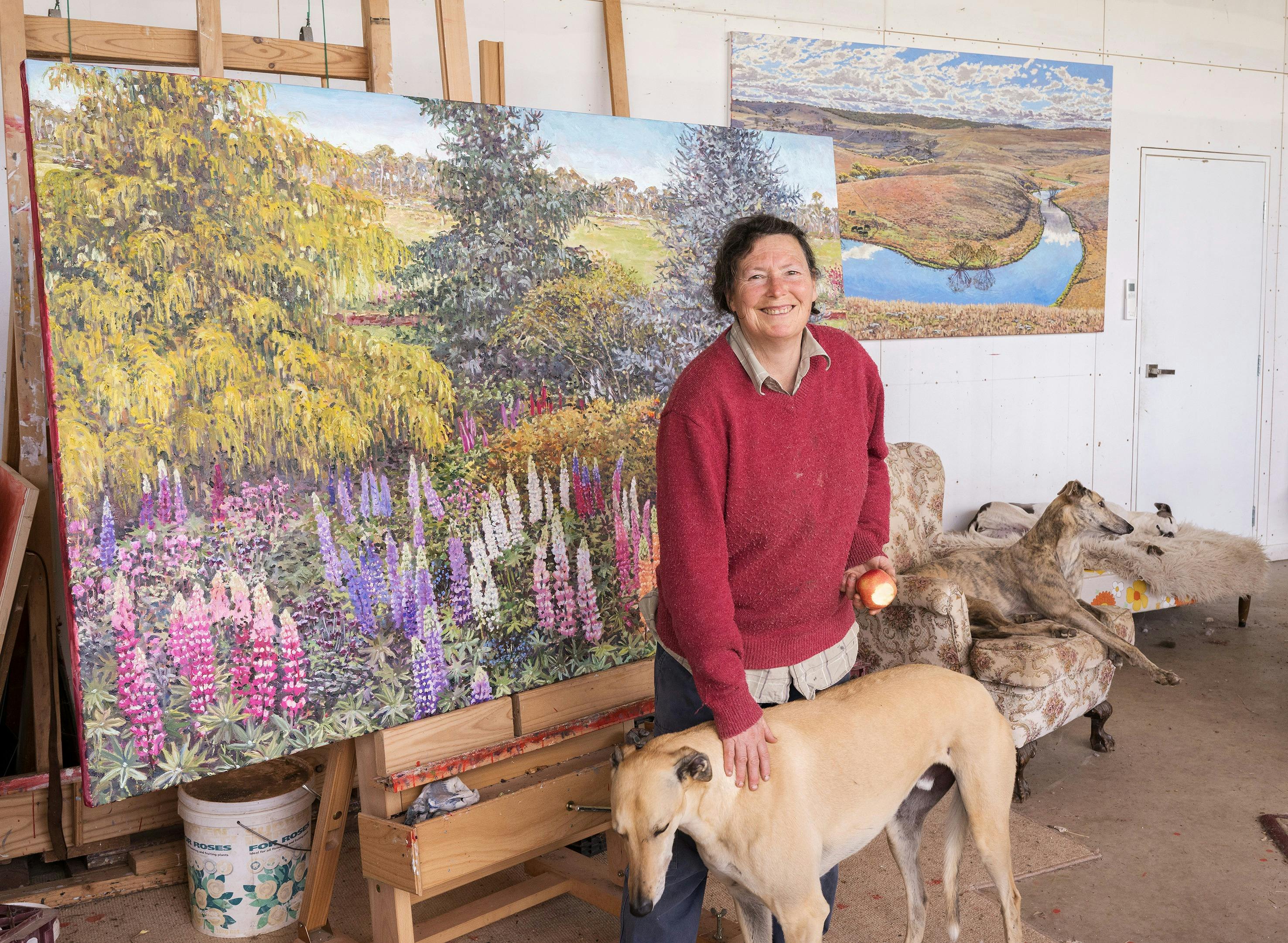 The artist Lucy Culliton stands smiling in her studio in front of 'Bibbenluke Spring' artwork, 2025.